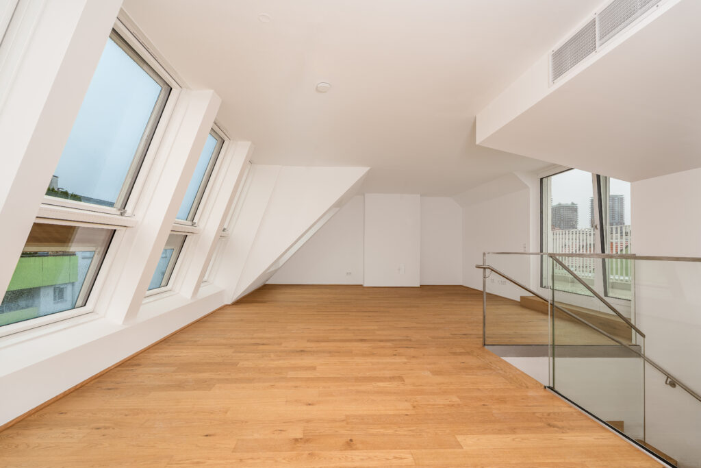 Heller Wohnraum einer Dachgeschosswohnung in Wien mit großer Dachfenster-Kombination und Glasgeländer